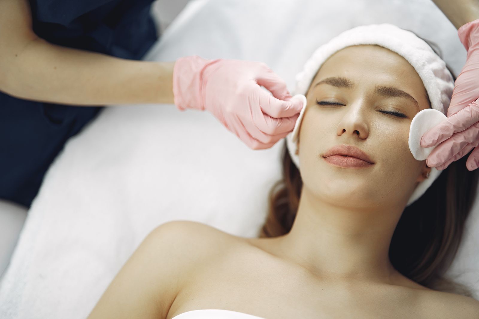 Cliente recebendo tratamento facial com toalha e algodão, ambiente calmo
